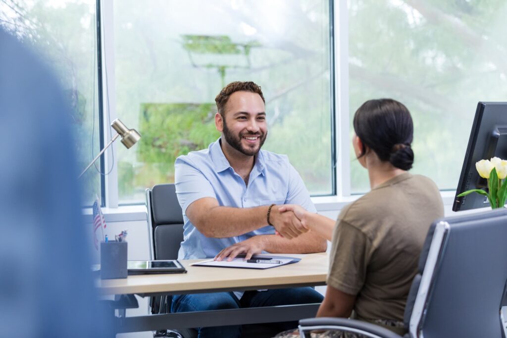 Hiring manager shaking hands with a job candidate across a desk during an interview.