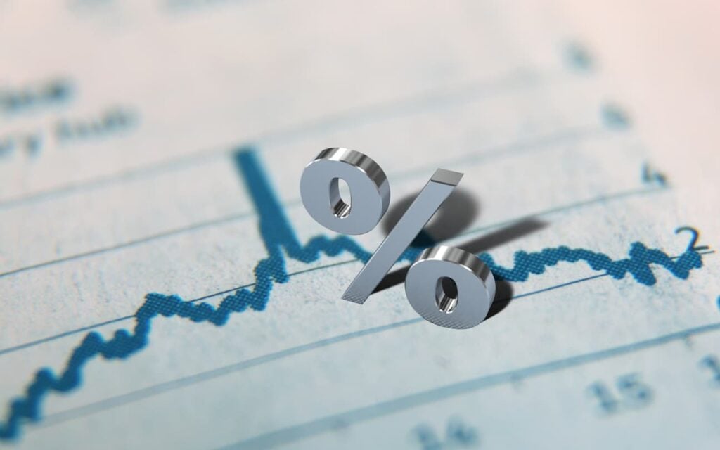 A 3D percent sign casts a shadow over a rising line chart on a financial document, representing interest rate trends.