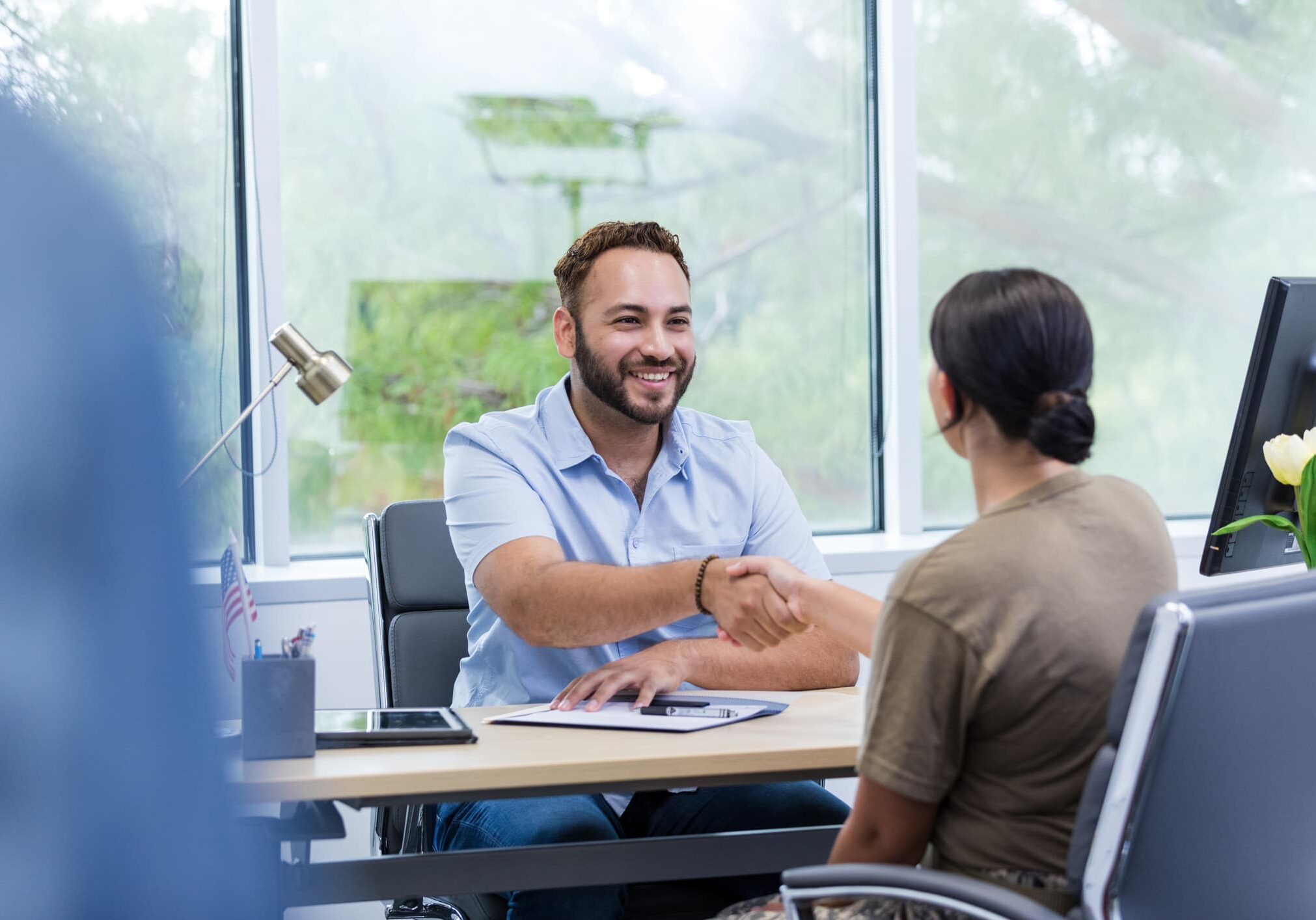 Hiring manager shaking hands with a job candidate across a desk during an interview.