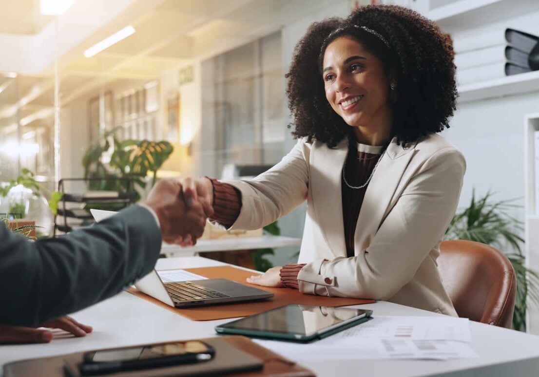 Hiring manager shaking hands with a job candidate across a desk in a modern office setting